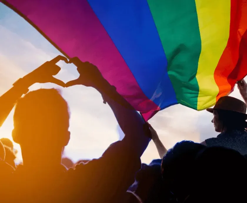 Shadow of a person making a heart with their hands, under a rainbow flag